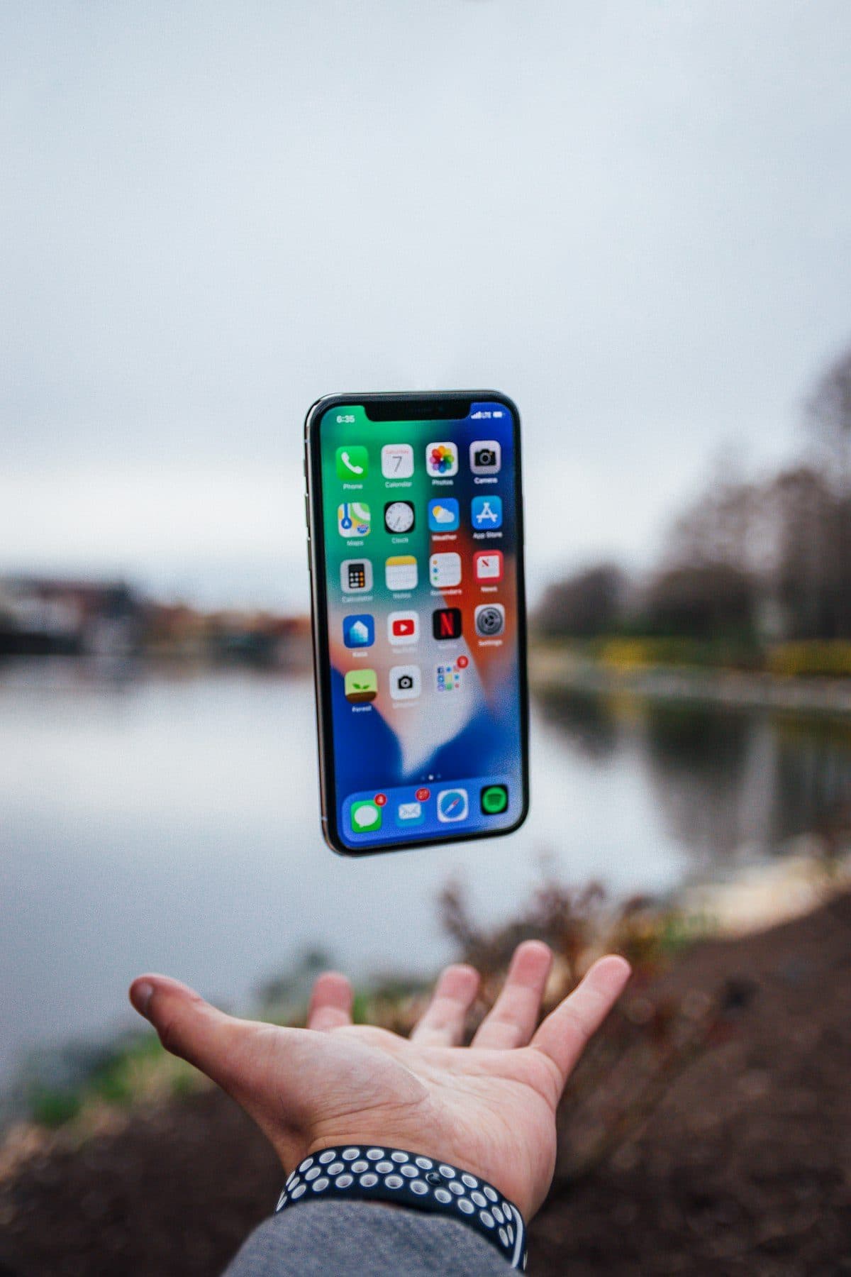 Une main tendant un téléphone au bord d'un lac